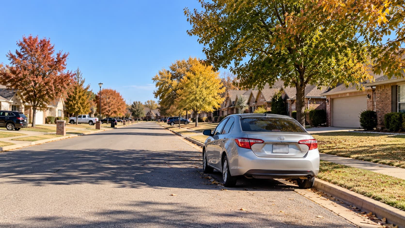 Silver sedan parked along a quiet suburban street with brick homes and fall trees in Oklahoma.